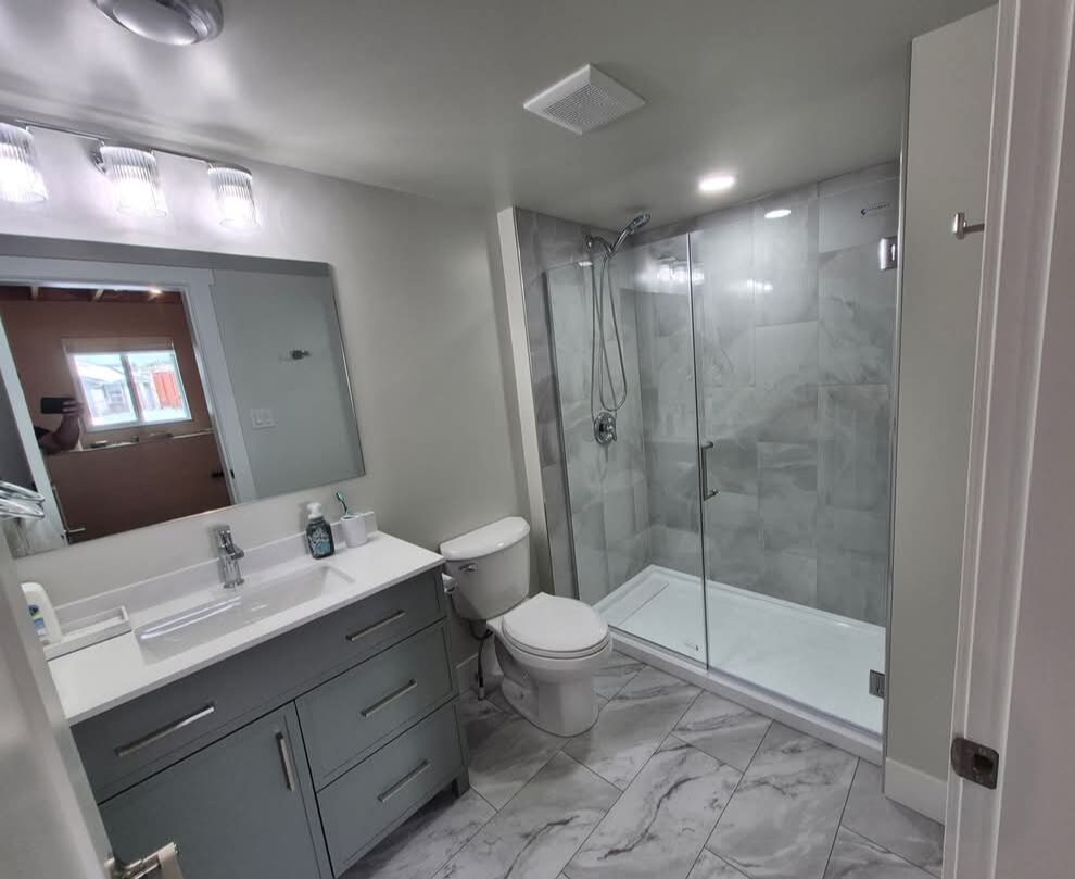Garret's Handyman & Renovation Services — Renovated bathroom with glass shower, vanity and marble-look tile floor